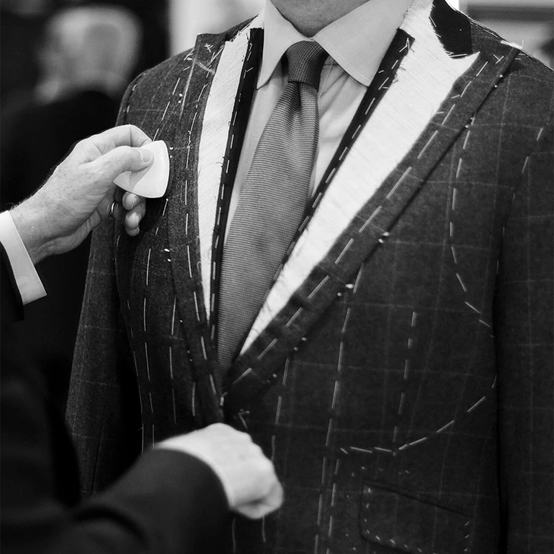 Client trying on an unfinished baste-fitted suit jacket with pins and chalk marks